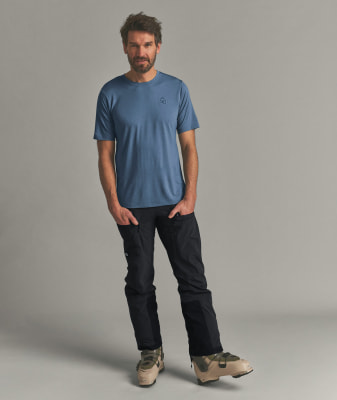 Ein Mann in einem blauen T-Shirt und schwarzer Hose mit Skischuhen.
