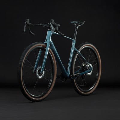 Modernes Gravelbike mit blaugrünem Rahmen und braunen Reifen vor dunklem Hintergrund.