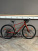 Ein orangefarbenes Gravelbike steht auf einem Holzboden vor einer grauen Wand.