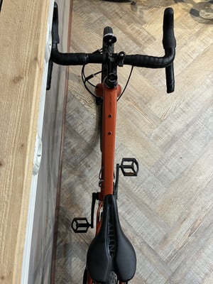 Orangefarbenes Gravelbike mit schwarzem Lenker und Sattel auf Holzboden. Orangefarbenes Gravelbike mit schwarzem Lenker und Sattel auf Holzboden.