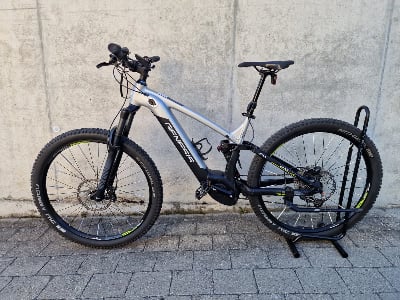 Ein Genesis E-Mountainbike steht auf Pflastersteinen vor einer Betonwand.