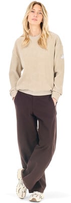 Eine Frau in einem beige Pullover und braunen Hosen mit Händen in den Taschen. Eine Frau in einem beige Pullover und braunen Hosen mit Händen in den Taschen.