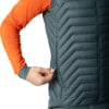 Ein Mann schließt eine dunkelgraue Daunenweste über einer orangefarbenen Jacke.