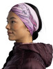 Eine Frau trägt ein rosa Buff-Stirnband und eine dunkelweine Jacke.