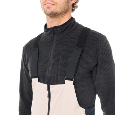 Ein Mann in einem schwarzen Fleece-Oberteil und einer hellen Latzhose. Ein Mann in einem schwarzen Fleece-Oberteil und einer hellen Latzhose.