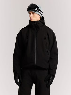 Ein Mann in einer Skijacke, Mütze und Skibrille mit Handschuhen vor grauem Hintergrund. Ein Mann in einer Skijacke, Mütze und Skibrille mit Handschuhen vor grauem Hintergrund.