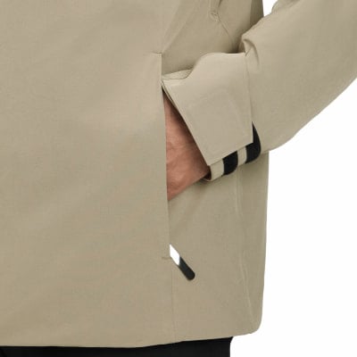 Eine Hand steckt in der Tasche einer beigefarbenen Jacke mit schwarzen Streifen am Ärmel. Eine Hand steckt in der Tasche einer beigefarbenen Jacke mit schwarzen Streifen am Ärmel.