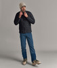 Ein Mann in einer Daunenjacke und Skihose mit Skischuhen.