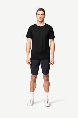 Ein Mann in einem schwarzen T-Shirt und dunklen Shorts steht vor einem weißen Hintergrund.