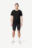 Ein Mann in einem schwarzen T-Shirt und dunklen Shorts steht vor einem weißen Hintergrund.