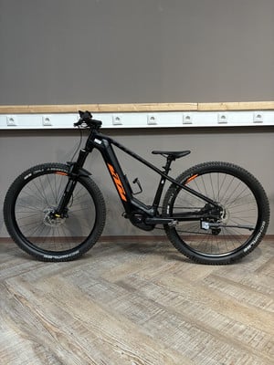 Schwarzes KTM E-Bike mit orangefarbenen Details auf Holzboden. Schwarzes KTM E-Bike mit orangefarbenen Details auf Holzboden.