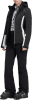 Eine Frau in einer schwarzen Skijacke und Hose mit weißen Details und Skischuhen.