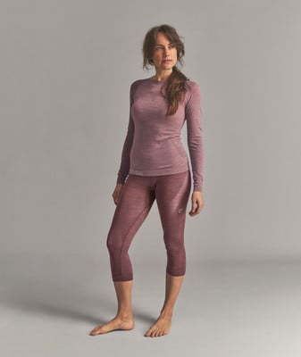 Eine Frau in einem weinroten Langarmshirt und 3/4-Leggings steht vor grauem Hintergrund. Eine Frau in einem weinroten Langarmshirt und 3/4-Leggings steht vor grauem Hintergrund.