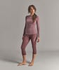 Eine Frau in einem weinroten Langarmshirt und 3/4-Leggings steht vor grauem Hintergrund.