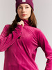 Frau in einem pinken Rollkragenpullover und lila Mütze mit Zopfmuster.