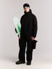 Ein junger Mann in schwarzer Snowboardkleidung hält ein Snowboard mit Grafikdruck.