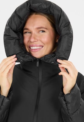 Eine Frau in einer schwarzen Daunenjacke mit Kapuze lächelt. Eine Frau in einer schwarzen Daunenjacke mit Kapuze lächelt.