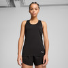 Eine Frau in einem schwarzen Sport-Tanktop und Shorts posiert vor einem grauen Hintergrund.