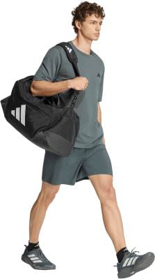 Ein Mann in dunkelgrauer Kleidung trägt eine schwarze Sporttasche über der Schulter. Ein Mann in dunkelgrauer Kleidung trägt eine schwarze Sporttasche über der Schulter.