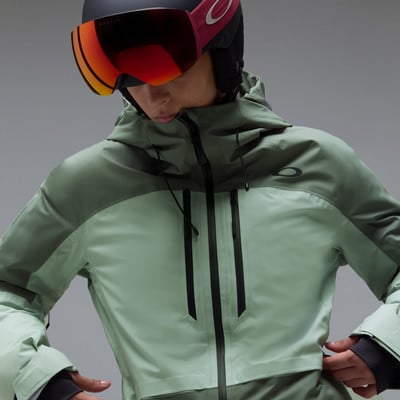 Eine Skifahrerin in einer grünen Jacke und Oakley-Brille blickt nach unten.