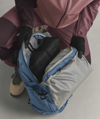 Eine Person in Handschuhen packt Kleidung in einen blauen Rucksack.