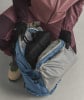 Eine Person in Handschuhen packt Kleidung in einen blauen Rucksack.