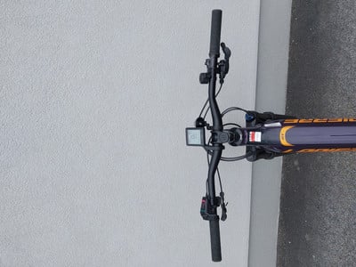 Lenker eines E-Bikes mit Display und Bedienelementen auf grauem Hintergrund.
