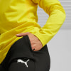 Ein Mann im gelben Pullover steckt seine Hand in die Tasche einer schwarzen Hose mit Puma-Logo.