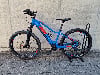 Ein blaues Mountain-E-Bike mit roten Akzenten auf einem Ständer vor einer Wand.