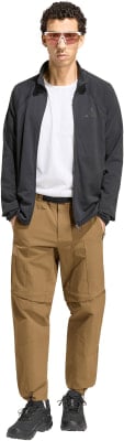 Ein Mann in dunkler Jacke, weißem T-Shirt und brauner Hose mit pinker Brille.