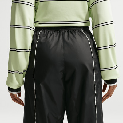 Grüner Pullover mit Streifen und schwarze Hose mit weißem Besatz.