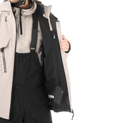 Ein Mann in einer beigen Jacke und schwarzer Latzhose mit offener Jacke. Ein Mann in einer beigen Jacke und schwarzer Latzhose mit offener Jacke.