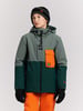 Ein Junge in einer Winterjacke und orangefarbener Hose mit Mütze.