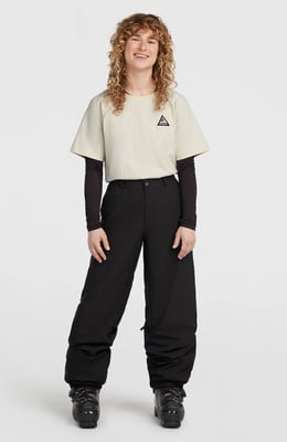 Frau in beige T-Shirt, schwarzer Skihose und Skischuhen.