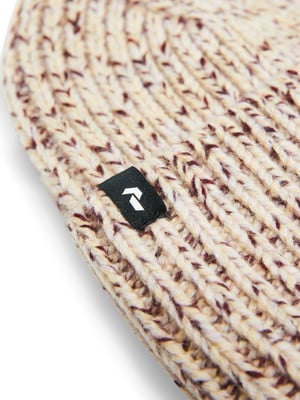 Detail einer Strickmütze mit hellen und dunklen Fasern und einem Logo.