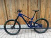 Ein blaues Mountainbike mit Federung steht vor einer Holzwand.