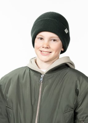 Ein Junge in einer grünen Jacke und Mütze lächelt in die Kamera.
