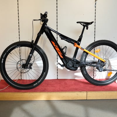 Schwarzes KTM E-Bike mit orangefarbenen Akzenten auf rotem Teppich. Schwarzes KTM E-Bike mit orangefarbenen Akzenten auf rotem Teppich.