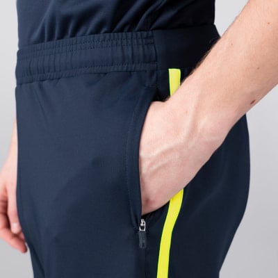 Detail einer dunkelblauen Sporthose mit Reißverschlusstasche und gelbem Streifen.