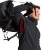 Ein Mann zieht einen Rucksack auf den Rücken, er trägt eine schwarze Jacke mit rotem Futter.