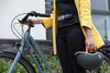 Frau in gelber Jacke hält Fahrrad und Helm.