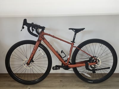 Ein braunes Gravelbike mit schwarzen Rädern und schwarzem Sattel steht auf einem Holzboden. Ein braunes Gravelbike mit schwarzen Rädern und schwarzem Sattel steht auf einem Holzboden.