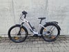 Ein silbernes E-Bike mit Gepäckträger steht vor einer Betonwand.