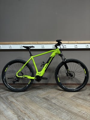 Ein grünes Elektro-Mountainbike steht auf einem Holzboden vor einer grauen Wand. Ein grünes Elektro-Mountainbike steht auf einem Holzboden vor einer grauen Wand.