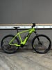Ein grünes Elektro-Mountainbike steht auf einem Holzboden vor einer grauen Wand.