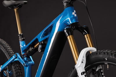 Detail eines blauen Mountainbike-Rahmens mit goldenen Stoßdämpfern und schwarzer Sattelstütze. Detail eines blauen Mountainbike-Rahmens mit goldenen Stoßdämpfern und schwarzer Sattelstütze.