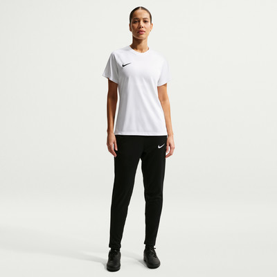 Eine Frau in einem weißen Nike-T-Shirt und schwarzer Hose steht vor einem weißen Hintergrund.