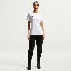 Eine Frau in einem weißen Nike-T-Shirt und schwarzer Hose steht vor einem weißen Hintergrund.