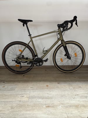 Ein grünes Gravelbike steht auf einem Holzboden vor einer weißen Wand. Ein grünes Gravelbike steht auf einem Holzboden vor einer weißen Wand.