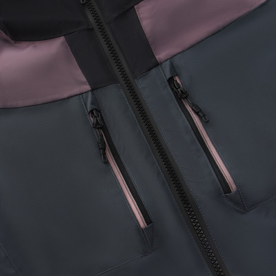 Detail zweier Reißverschlusstaschen auf einer dunklen Jacke mit Farbblöcken. Detail zweier Reißverschlusstaschen auf einer dunklen Jacke mit Farbblöcken.